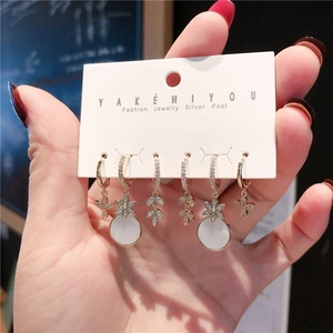 Detailed set of three gold earrings with zircons, flowers, and silver posts on display