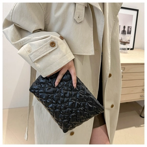 Detail of a black quilted cloud pouch with diamond pattern held by a woman in a trench coat