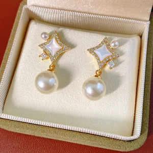 Détail de boucles d'oreilles étoile dorées avec incrustation blanche et perle ronde