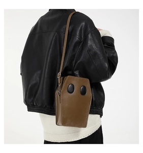 Brown coffin-shaped crossbody bag featuring cute cartoon ghost face details worn by model