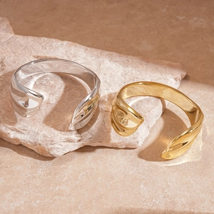 Close-up of gold and silver pleated cuff bracelets with fluid metallic texture on stone