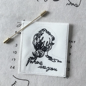Detail of fabric embroidery pin with black portrait sketch and gold safety pin