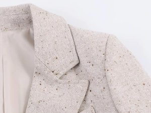 Gros plan sur la texture du tweed avoine et les coutures d'épaule précises d'un blazer