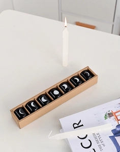 Close-up of 7-piece black ceramic moon phase candle holders in a long cardboard box