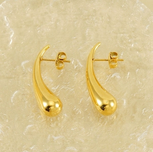 Close-up of polished golden teardrop earrings on a textured frosted glass background