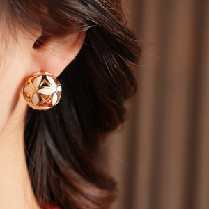 Gros plan d'un mannequin portant des boucles d'oreilles boules dorées et émail blanc
