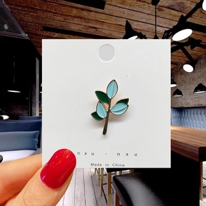 Detailed close-up of a leaf enamel pin in blue and green with gold plating on card