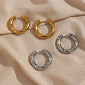 Polished thick hoop earrings in gold and silver finish on soft satin fabric background