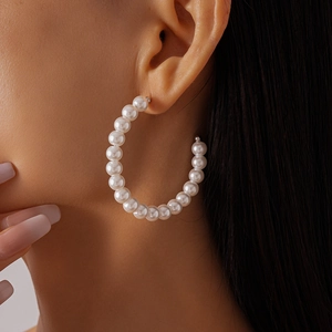 Macro detail of large C-shaped imitation pearl hoop earring worn by a model in warm light