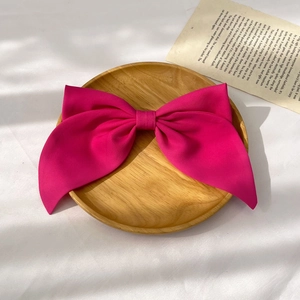 Detailed close-up of a large pink satin bow hair clip on a wooden tray with soft lighting