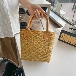Detail of hand-woven straw handbag featuring premium brown leather handles and rivets