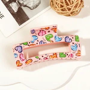 Detail of pink rectangular hair claw clip with colorful heart patterns on a stylish background
