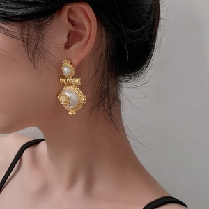 Close-up of vintage gold pearl earrings with floral relief on woman's ear