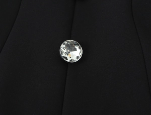 Macro detail of a faceted crystal button on premium black fabric for formal rompers