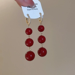 Detail of elegant gold-plated ear buckles with triple red resin bead tassels for women