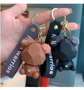 Detail of geometric teddy bear keychain with gold ring and rubber wrist strap in brown and black