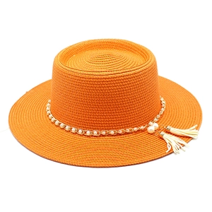 Détail d'un chapeau de paille orange avec chaîne dorée, perles et glands blancs