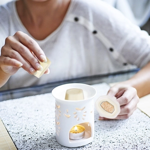 Woman placing soy wax melt into a white ceramic hollow burner for home aromatherapy