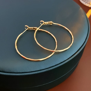 Detailed view of golden textured hoop earrings on a professional dark green display stand