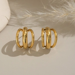 Détail de boucles d'oreilles géométriques dorées sur un fond décoratif beige doux