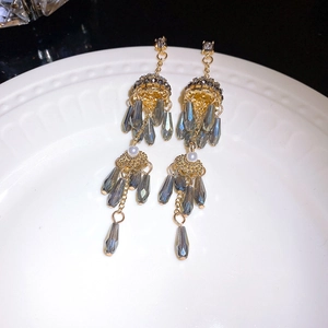 Gros plan de boucles d'oreilles pompons dorées avec perles grises et blanches sur plateau