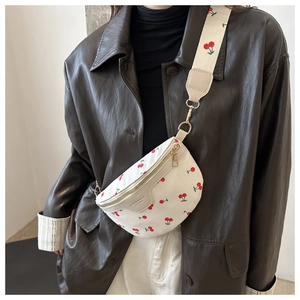 Detail of white cherry print crossbody bag with gold hardware and leather brand tag