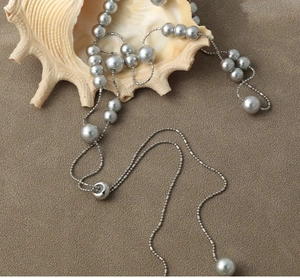 Detailed view of silver long pearl necklace draped elegantly over a large seashell