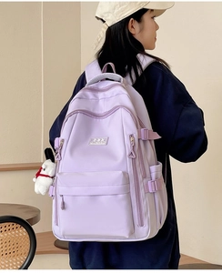 Rear view of a light purple durable nylon backpack with white puppy charm on a model