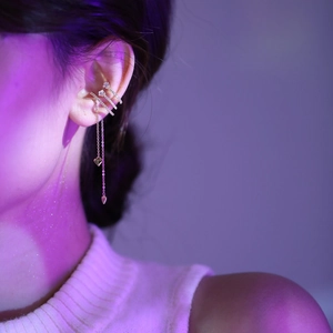 Detail of gold ear cuff with shimmering tassels and heart charms worn by a model