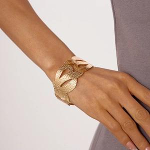 Dettaglio di un ampio bracciale rigido dorato con linee ondulate e texture sbalzata