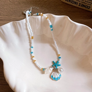 Detail of starfish and shell pendants on a pearl beaded necklace in a ceramic shell tray