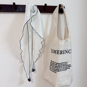 Detail of a beige canvas tote bag with letter print and a white scarf with grey trim