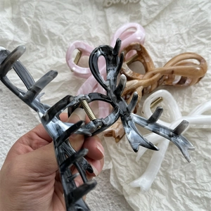 Large marble-patterned hair claws in black, pink, and brown displayed on beige fabric