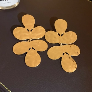 Detailed view of large gold floral earrings with hammer textured petals on leather