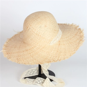Detail of handmade raffia sun hat featuring a fringed edge and delicate lace ribbon