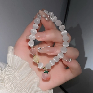 Nahaufnahme des Katzenaugen-Perlenarmbands mit rosa Pfirsichanhänger am Handgelenk