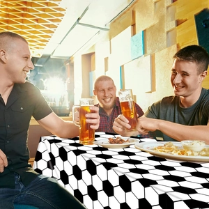 Men celebrating with beer at a table covered in a soccer-themed plastic tablecloth