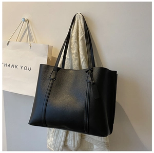 Detail of a black leather tote bag with long handles displayed against a neutral wall