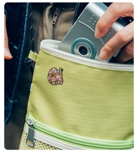 Detailed view of a cute sloth enamel pin on a green canvas bag with a silver camera