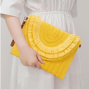 Detailed view of yellow woven raffia envelope clutch bag featuring round fringe and wrist strap