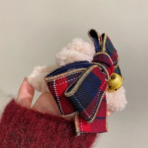 Detailed view of plush beige hair claw with red and green plaid bow and golden bell