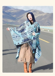 Blue geometric hooded poncho with tassels for travel, shown on a mountain road