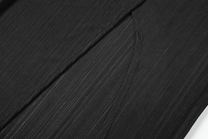 Detail view of the side slit and vertical pleated texture on a black long dress