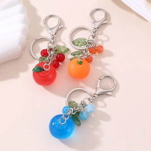 Close-up of colorful resin fruit keychains including red apple and orange on pink surface
