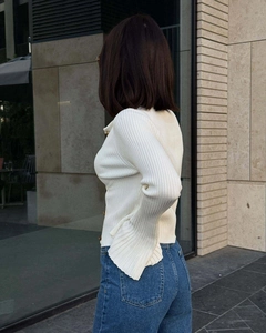 Detailed side view of white ribbed knit cardigan with gold buttons and flared sleeve cuffs
