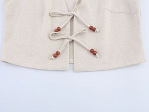 Dettaglio del gilet in lino beige con chiusura a lacci e perline di legno decorative