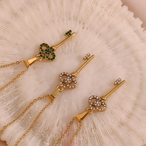 Detailed view of vintage hollow key pendants with green gems and pearls on gold chains