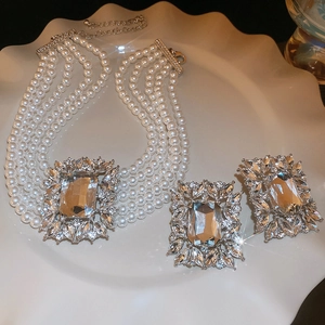 Detail of layered pearl necklace and square crystal earrings set on a ceramic tray