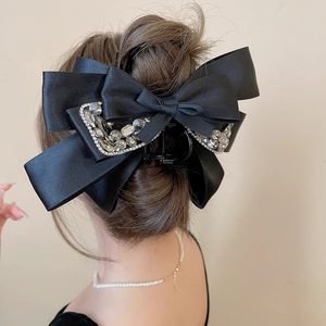 Detail of elegant black satin bow hair claw clip with sparkling rhinestones on model's hair
