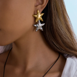 Polished star-shaped puff earrings in gold and silver finish on a model wearing white